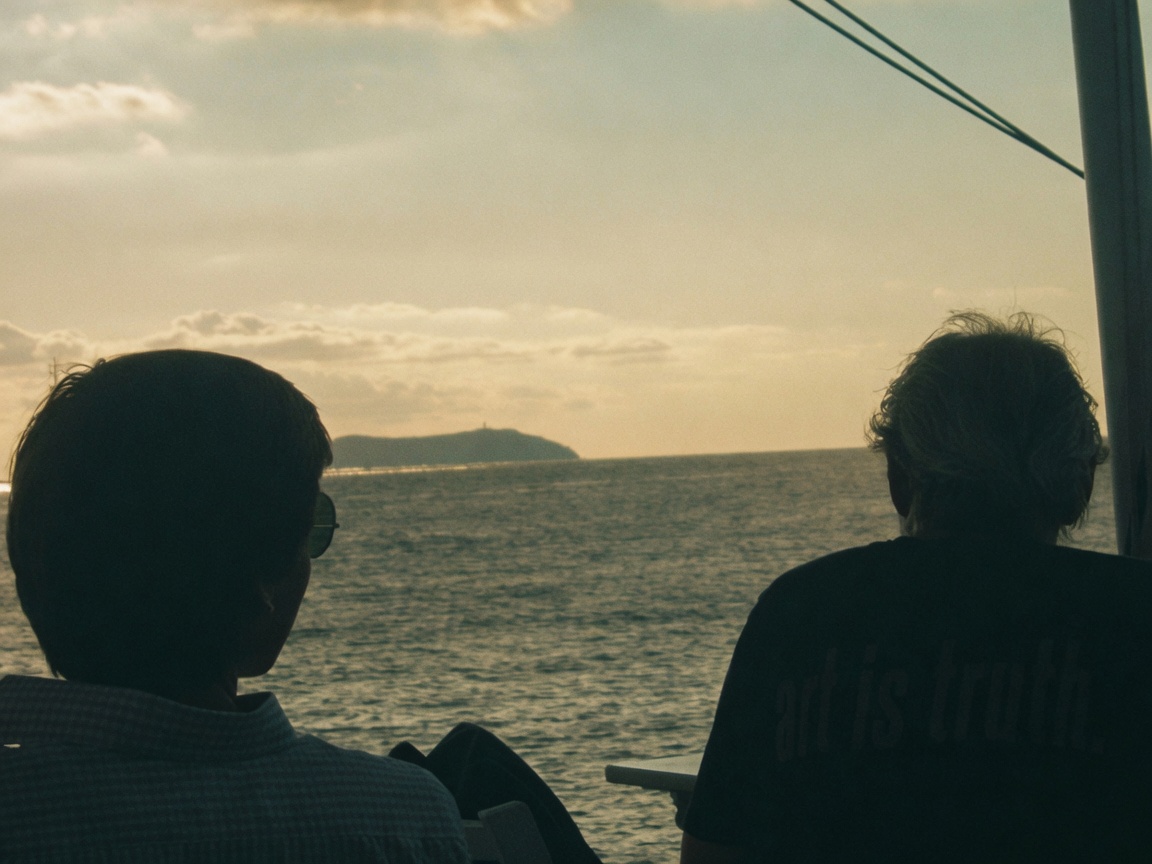 Two people on a boat looking toward the island across the water.