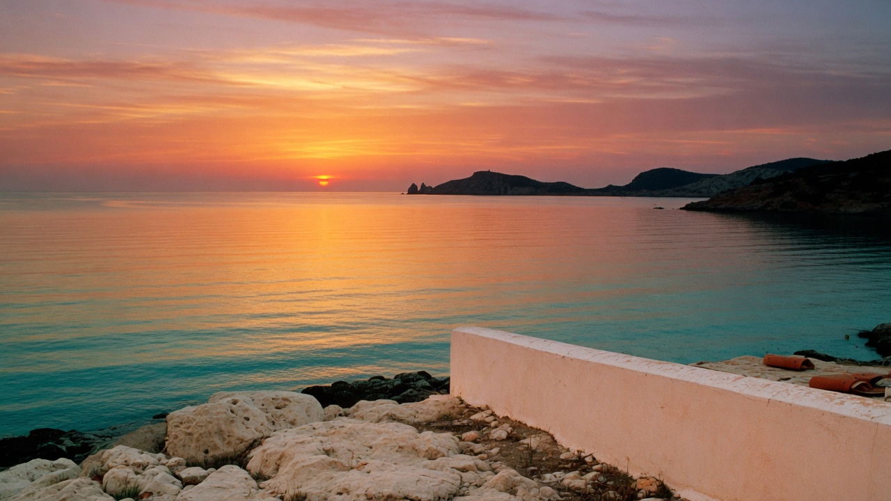 Sunset over the west coast of Ibiza, the sun touching a calm Mediterranean sea.